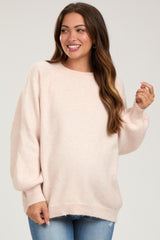 woman wearing a light pink maternity sweater with balloon sleeves and a relaxed fit, smiling and holding her baby bump