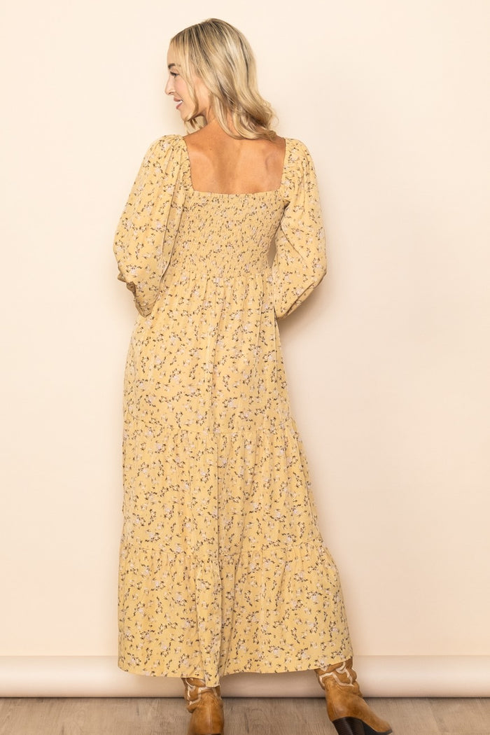 woman wearing a yellow floral maxi dress with a square neckline and puff sleeves, showing the back view