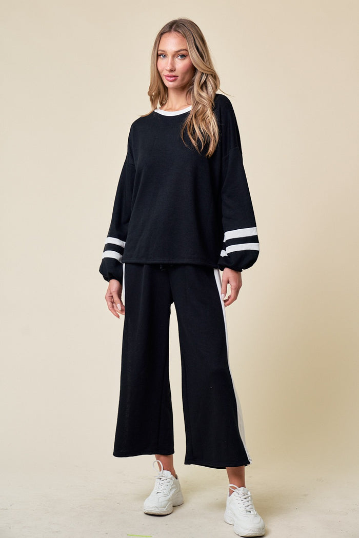 woman wearing a black lounge set with white stripes on the sleeves and pants, paired with white sneakers