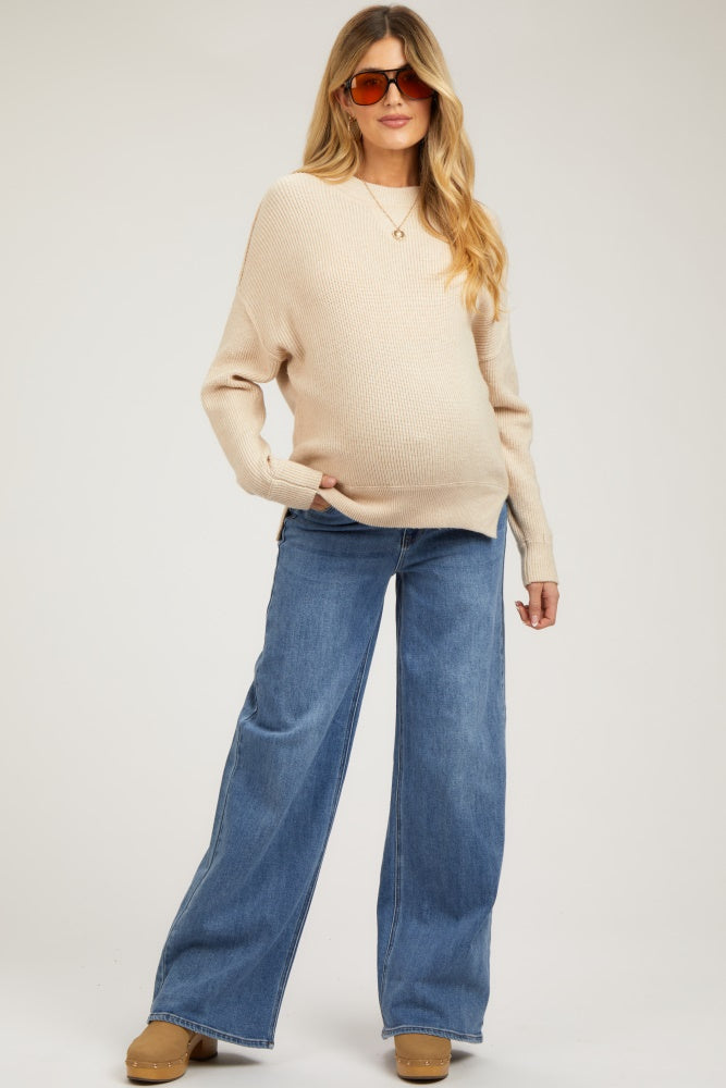woman wearing a beige ribbed maternity sweater and wide-leg jeans, showing a baby bump and styled with sunglasses