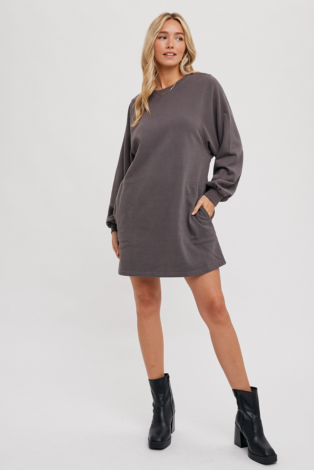 woman wearing a gray oversized sweatshirt dress with long sleeves and side pockets, paired with black ankle boots