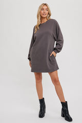 woman wearing a gray oversized sweatshirt dress with long sleeves and side pockets, paired with black ankle boots
