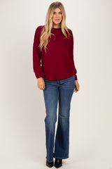 woman wearing a burgundy knitted sweater and blue flared jeans, standing with hands on hips