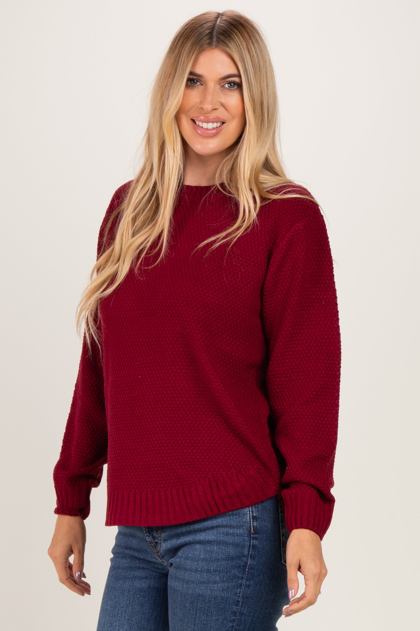 woman wearing a burgundy knitted sweater with long sleeves and a relaxed fit, paired with blue jeans