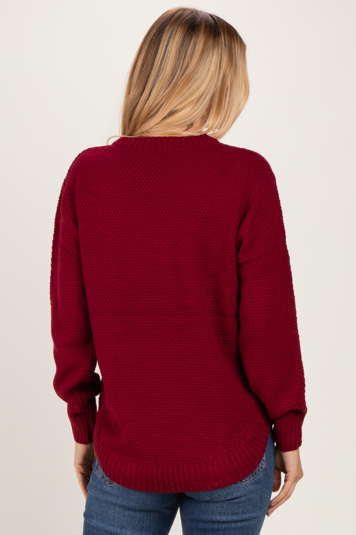woman wearing a burgundy chunky knit sweater with a round neckline and long sleeves, seen from the back