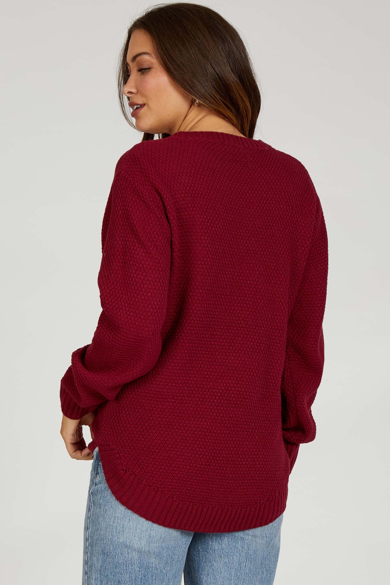 woman wearing a deep burgundy oversized knitted maternity sweater with long sleeves and side slits, viewed from the back