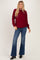woman wearing a burgundy oversized knit sweater and flared jeans, standing with one hand on her hip