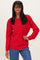 woman wearing a red textured sweater paired with blue jeans, smiling at the camera