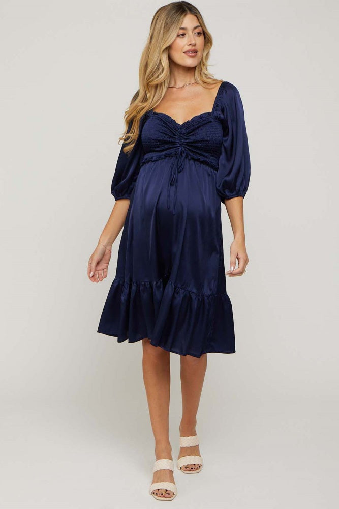 woman wearing a navy blue maternity dress with puff sleeves and a tiered ruffled hem, showing her baby bump