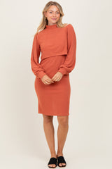 woman wearing a rust colored ribbed long sleeve dress with a fitted silhouette and curved hemline