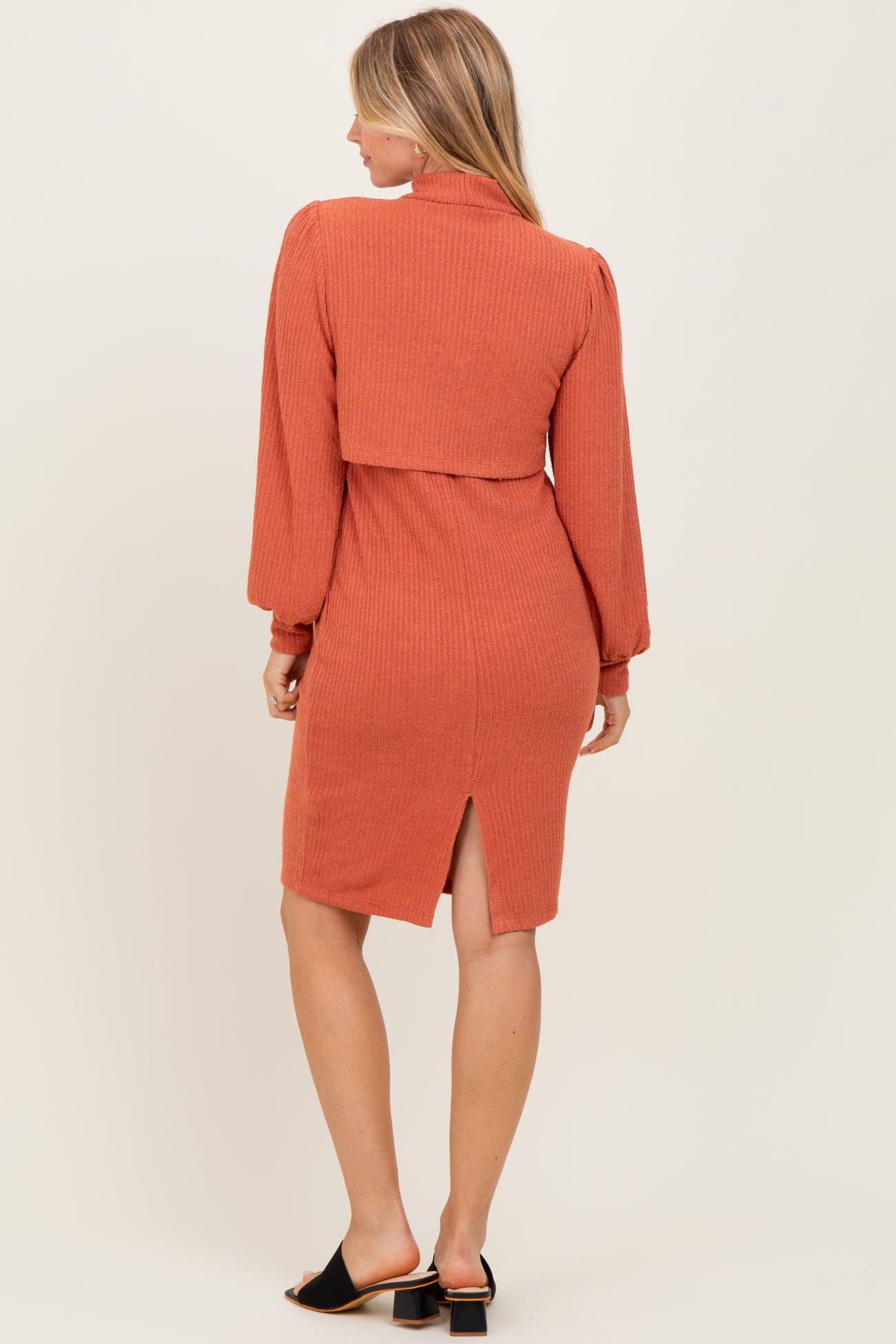 woman wearing a rust-colored ribbed midi dress with long sleeves and a back slit detail