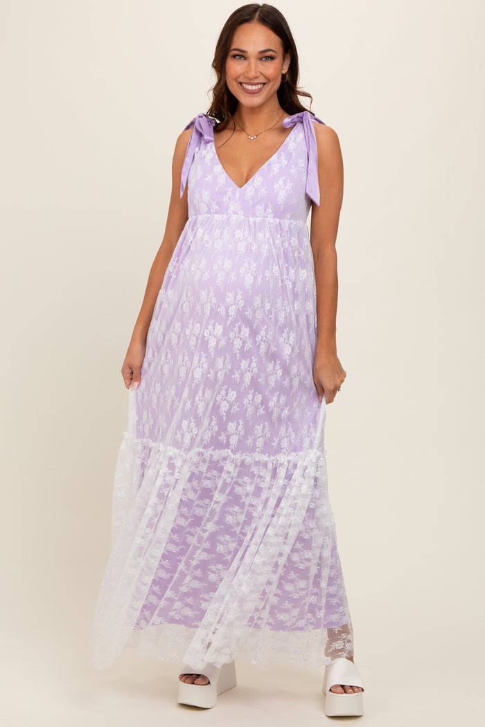 woman wearing a lavender maternity maxi dress with floral details and lace accents, holding the dress while smiling