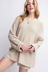 woman wearing a beige oversized knit sweater with long sleeves and a relaxed fit, styled with layered necklaces