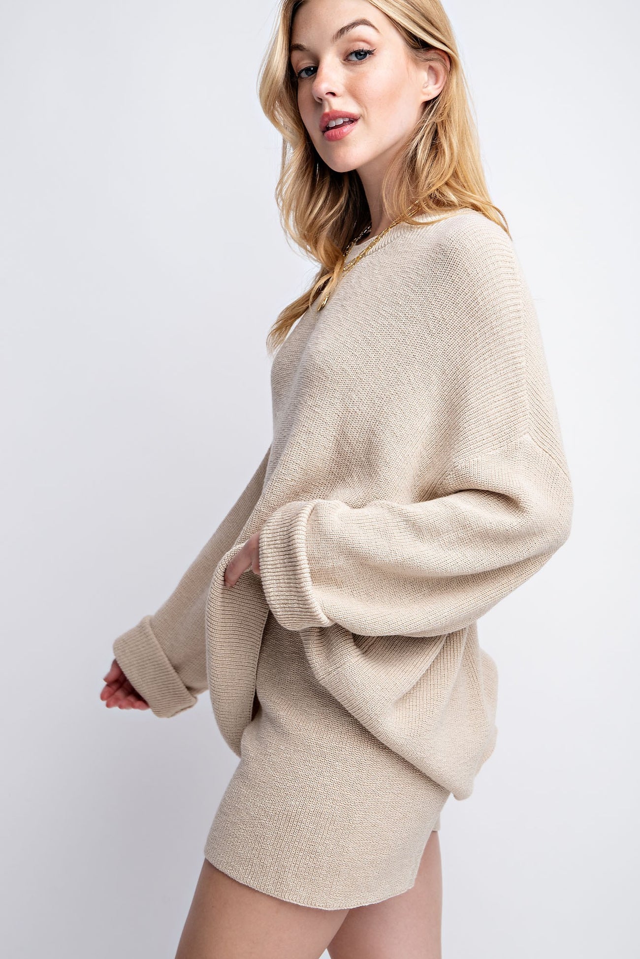 woman wearing a beige oversized sweater with long sleeves and a relaxed fit, standing sideways on a light background