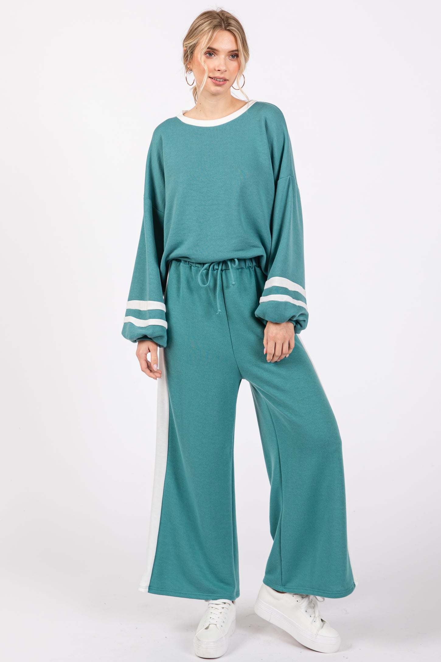 woman wearing a teal lounge set with balloon sleeves and white stripe details, standing against a white background