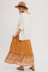 woman wearing a white oversized sweater and a mustard yellow patterned maxi skirt, paired with a tan hat
