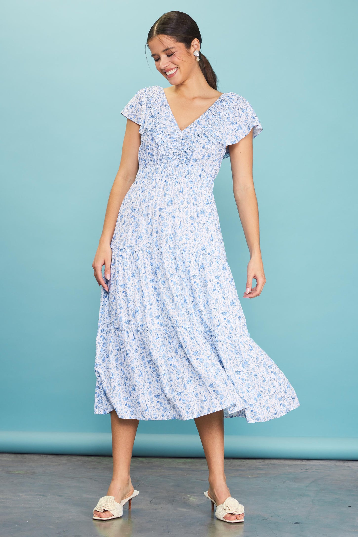 woman wearing a light blue floral maxi dress with short sleeves and a v-neckline, twirling against a blue background