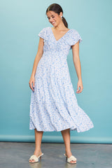 woman wearing a light blue floral maxi dress with short sleeves and a v-neckline, twirling against a blue background