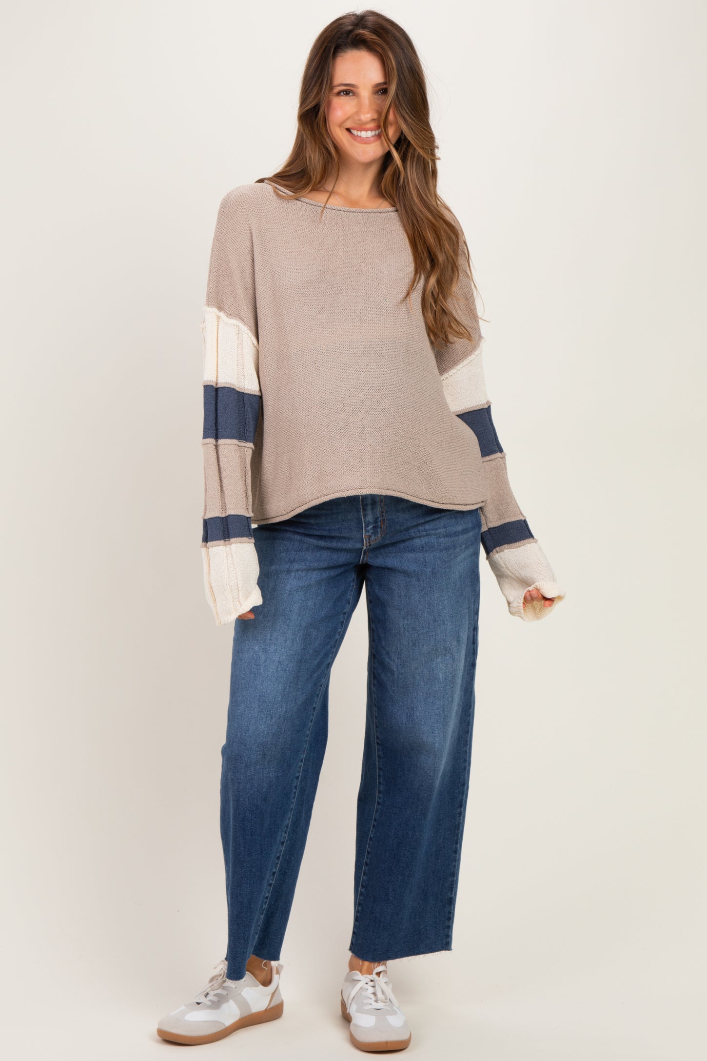 woman wearing a beige maternity sweater with navy and white stripes and blue wide-leg jeans, showing her baby bump