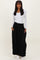 woman wearing a white ribbed long sleeve top and a black maxi skirt with pockets, standing against a neutral background