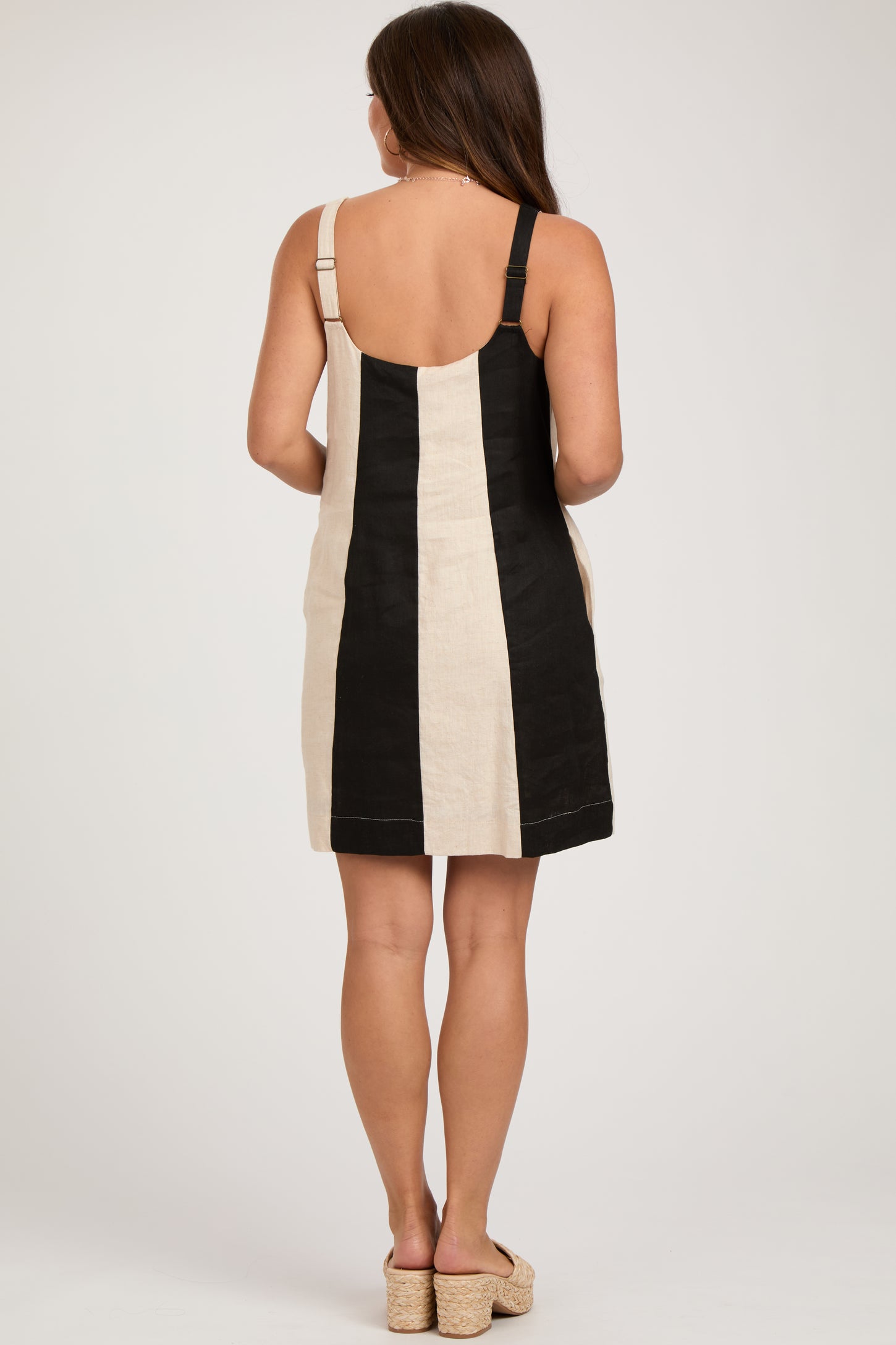 woman wearing a black and beige striped maternity dress with adjustable straps, showing her back