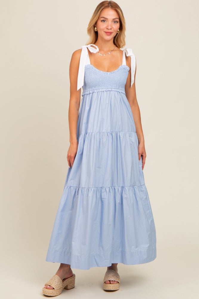 woman wearing a light blue tiered maxi dress with adjustable white tie straps and smocked bodice, standing on a neutral background