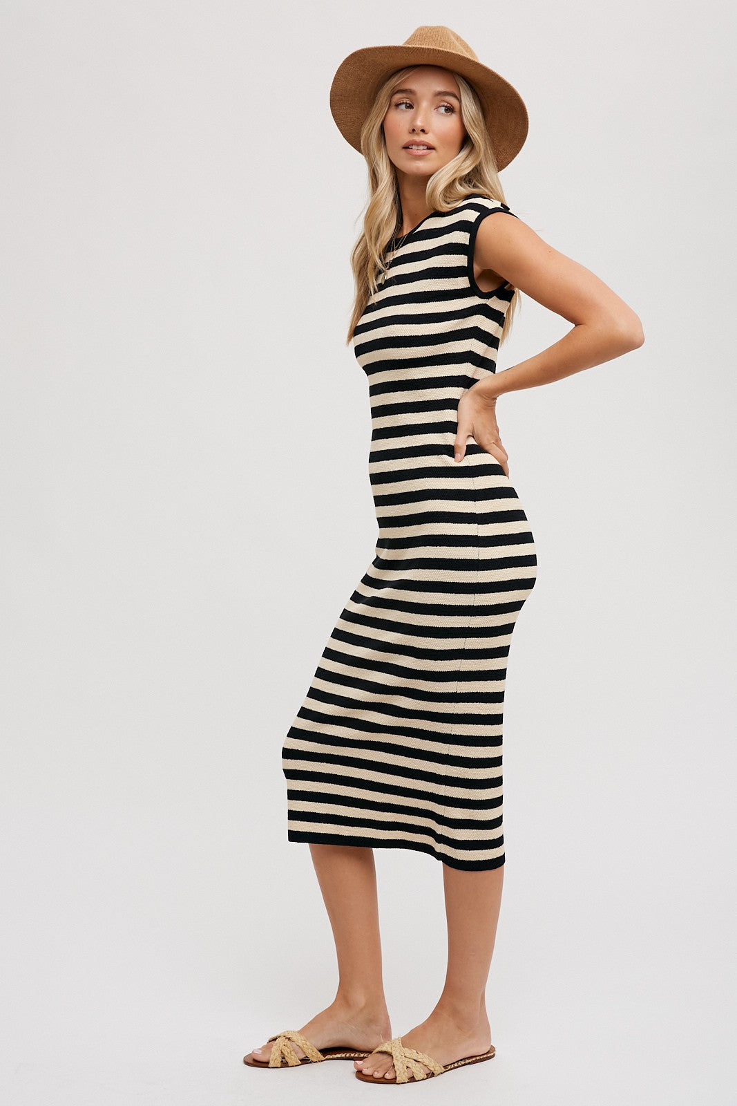 woman wearing a black and cream striped midi dress with short sleeves and a fitted silhouette, styled with a wide-brim hat and sandals