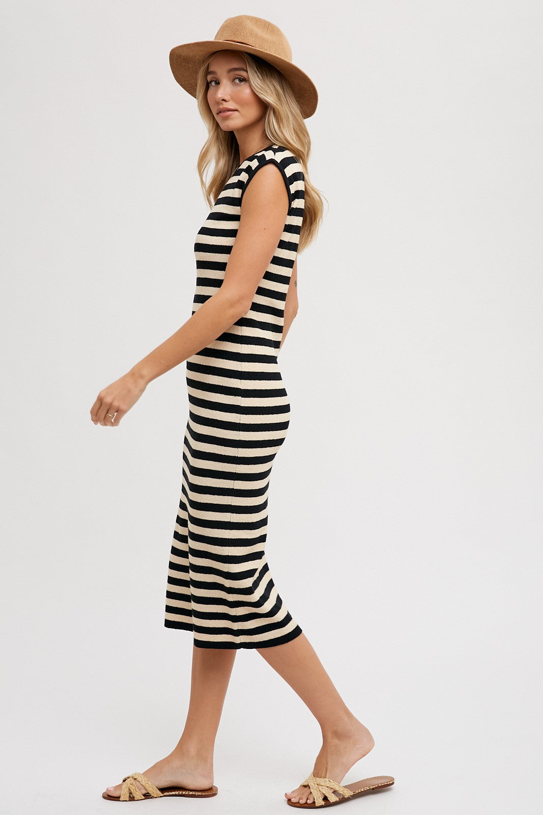 woman wearing a black and beige striped midi dress and a wide-brim hat, styled with flat sandals