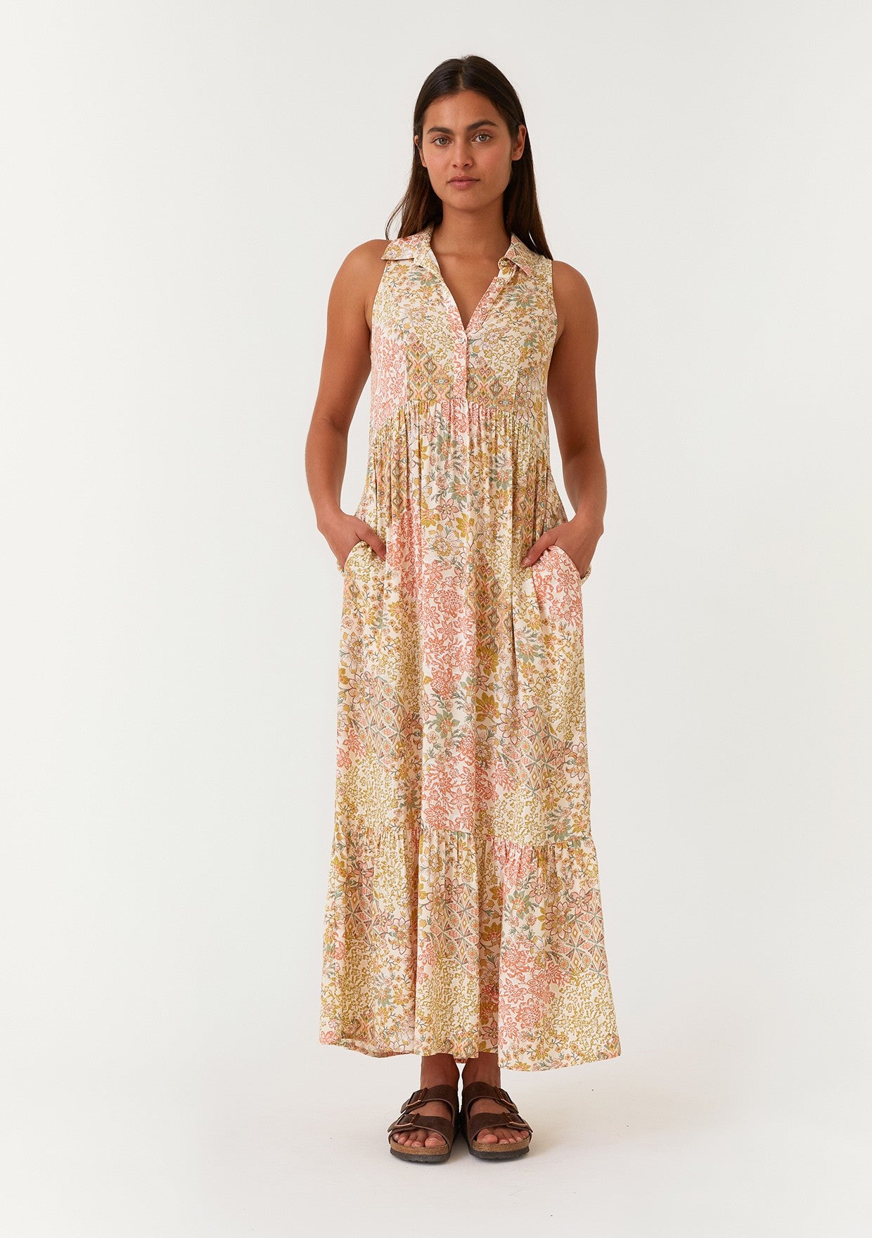 woman wearing a sleeveless floral maxi dress with a button-down front and pockets, standing against a plain background