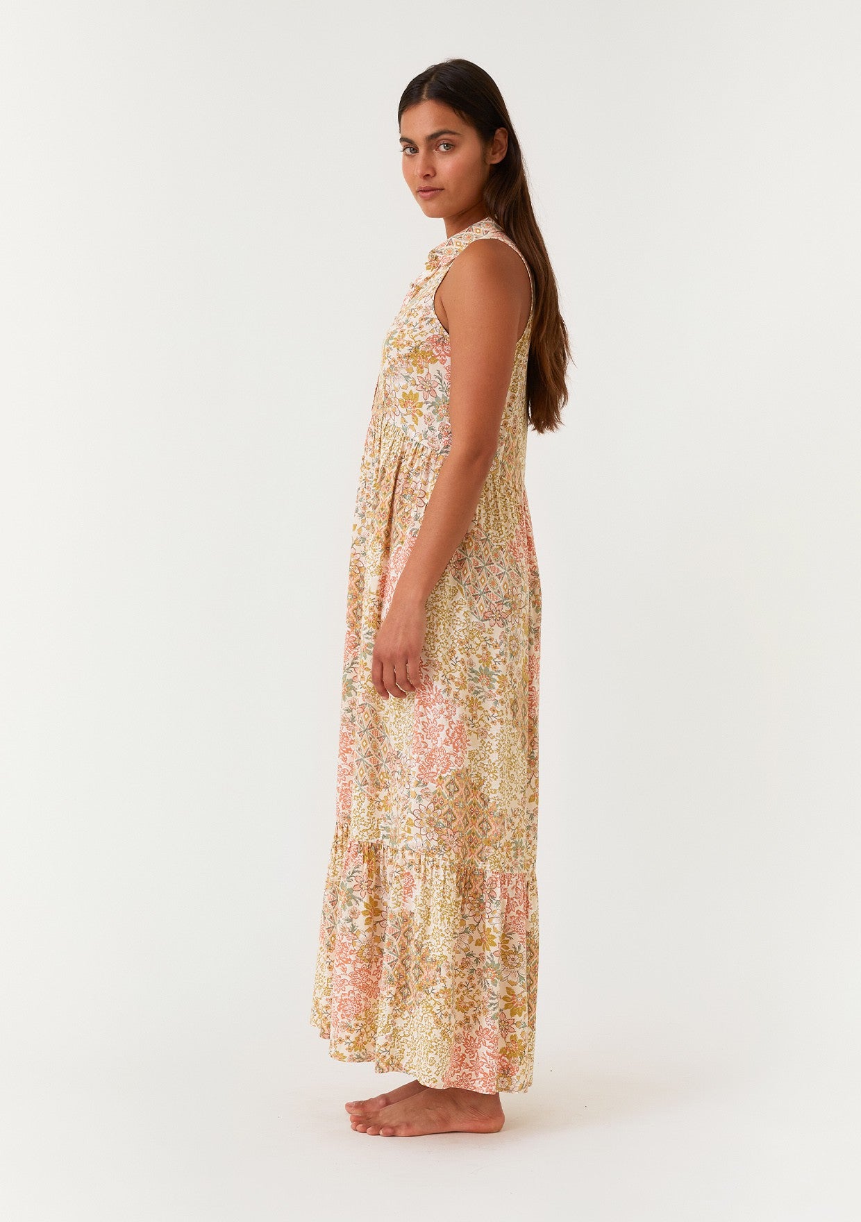 woman wearing a sleeveless floral maxi dress with a tiered skirt and ruffled neckline standing sideways