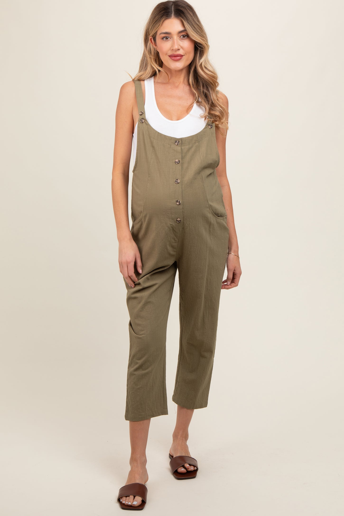 woman wearing olive green maternity overalls with buttons and a white tank top, showing her baby bump