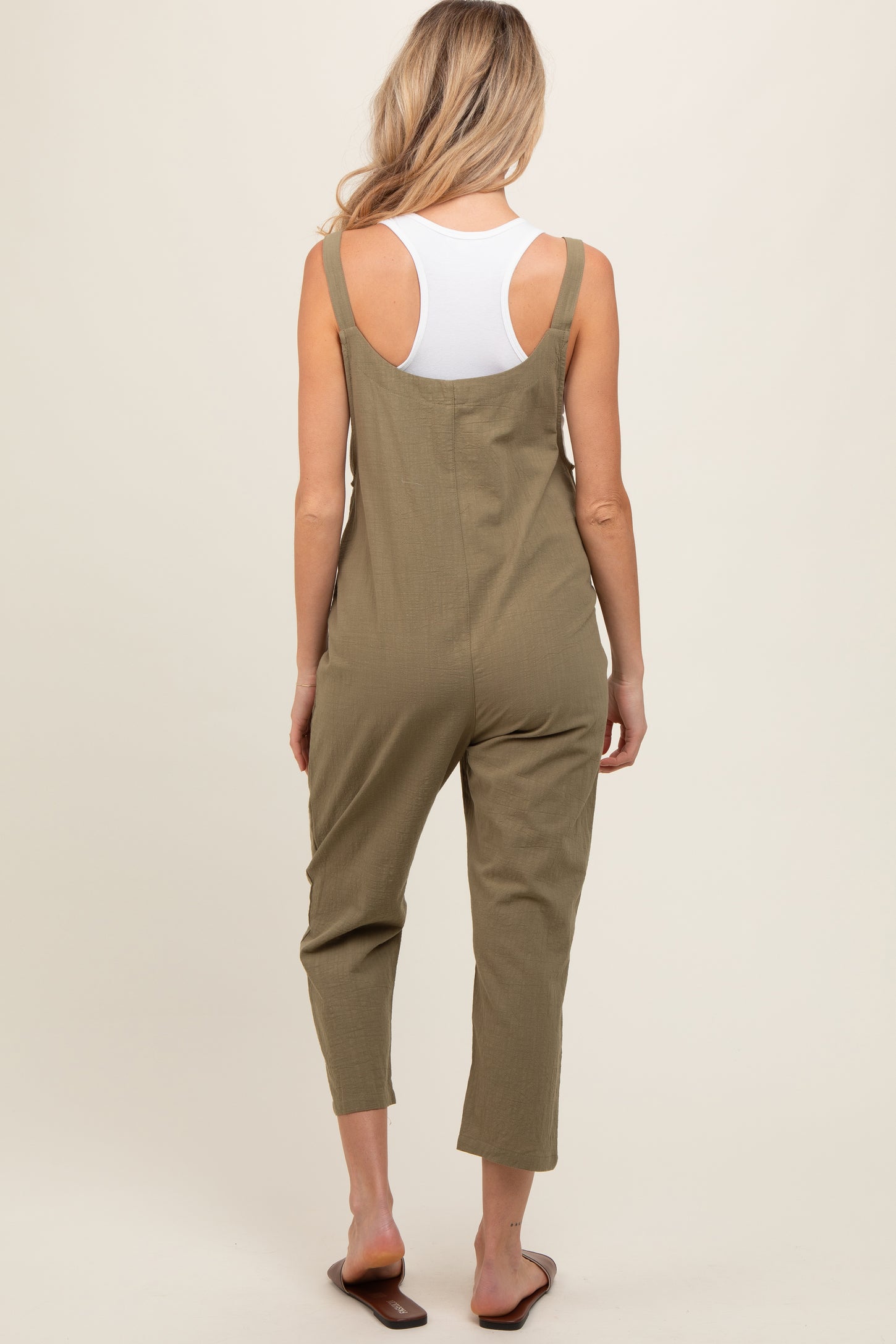 woman wearing an olive green maternity jumpsuit with adjustable straps and cropped legs, showing her back