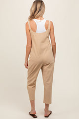 woman wearing a beige maternity jumpsuit with a relaxed fit and adjustable straps, seen from the back