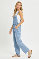 woman wearing light blue denim overalls with a white tank top and beige slide sandals