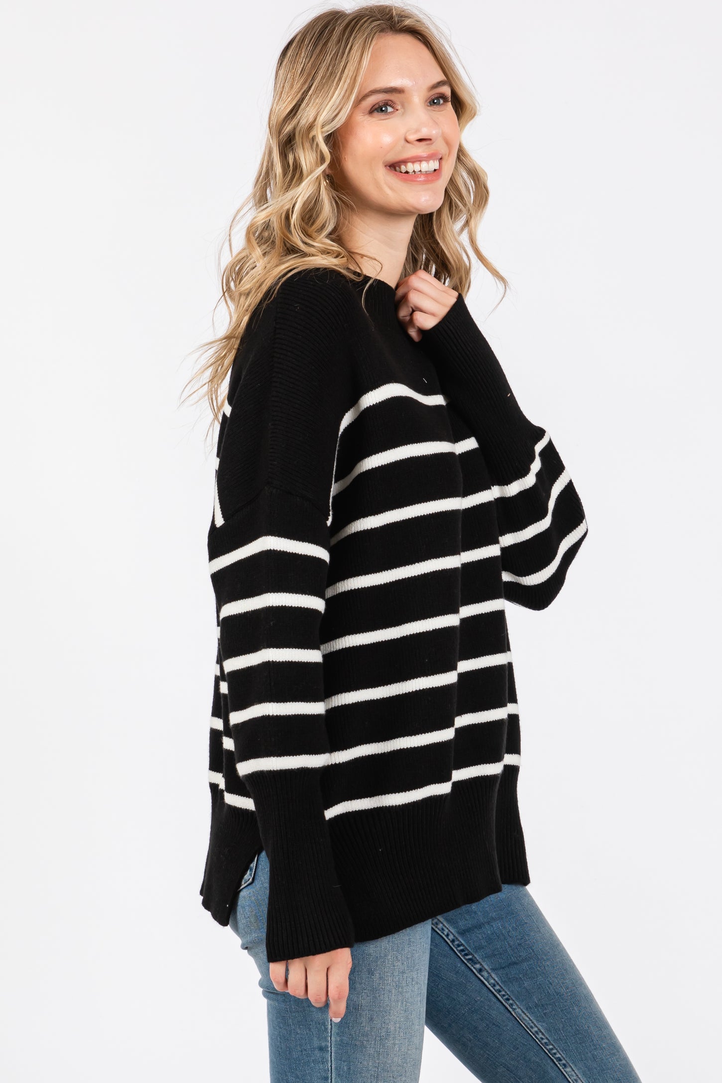 woman wearing a black and white striped oversized sweater with long sleeves and side slits, paired with blue jeans