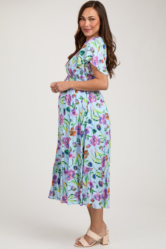 woman wearing a floral short sleeve maternity dress, showing her baby bump, in a light blue color with green accents
