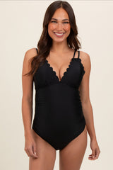 woman wearing a black scalloped edge maternity swimsuit with adjustable straps and a plunging neckline