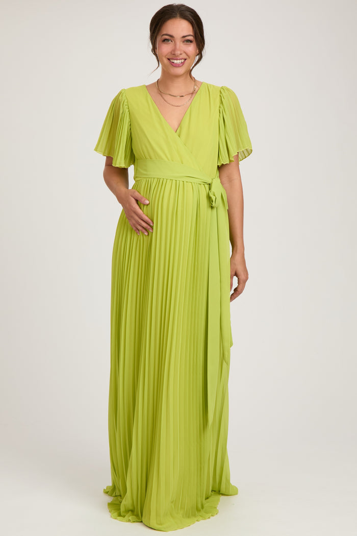 woman wearing a lime green pleated maternity wrap dress with short flutter sleeves and a tie waist, displaying her baby bump