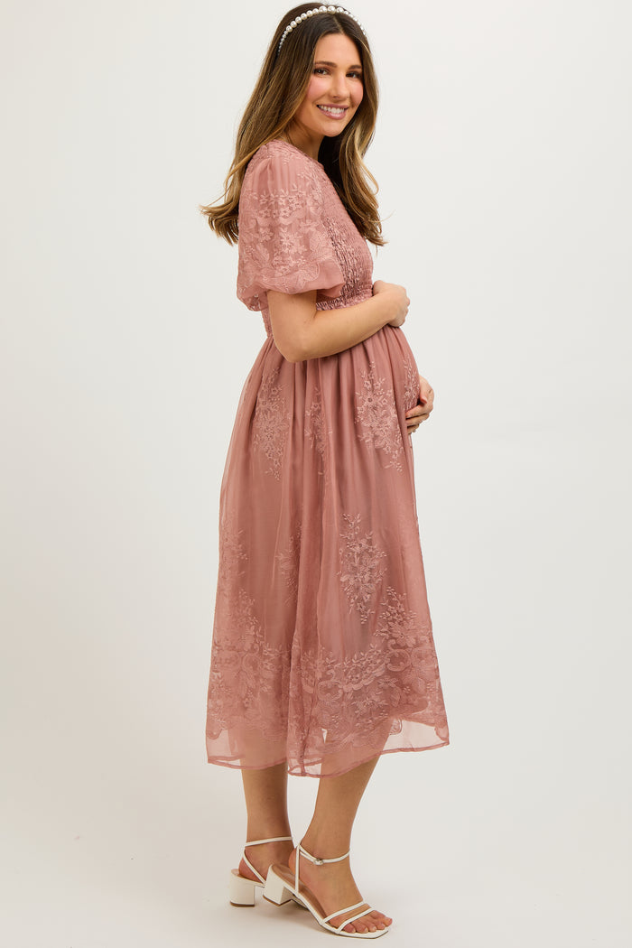 woman wearing a dusty rose maternity dress with floral embroidery and short sleeves, holding her baby bump