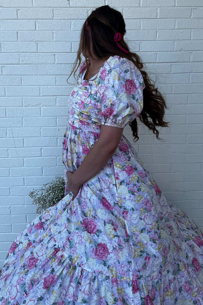 woman wearing a floral maternity dress with puff sleeves, holding her baby bump and facing away from the camera