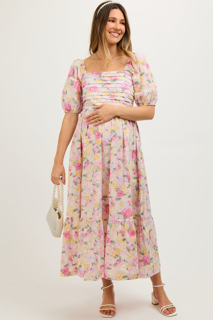 woman wearing a pink floral maternity dress with puff sleeves and a tiered skirt, holding her baby bump