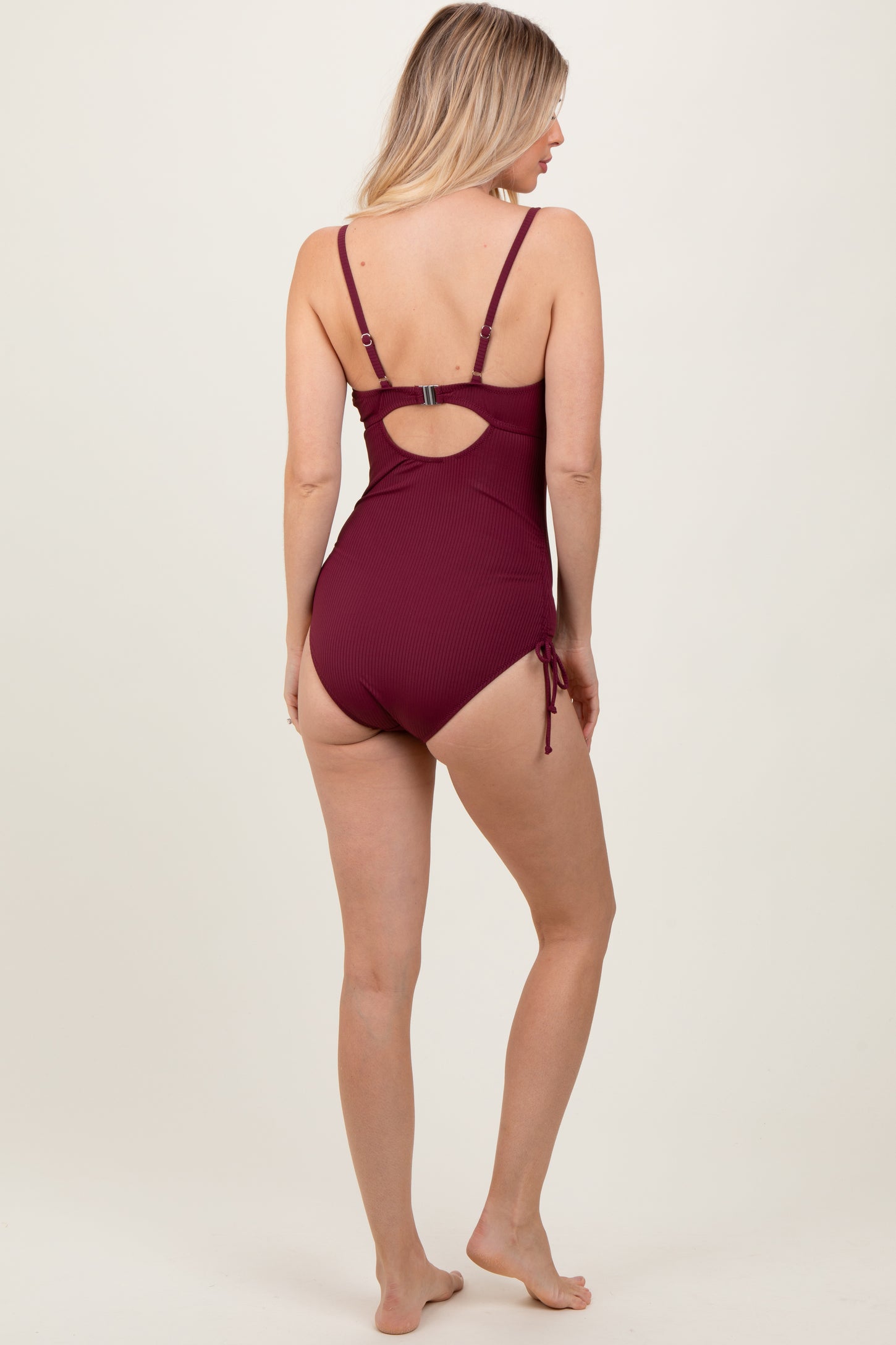 woman wearing a burgundy ribbed one-piece swimsuit with adjustable straps and side ties, viewed from the back