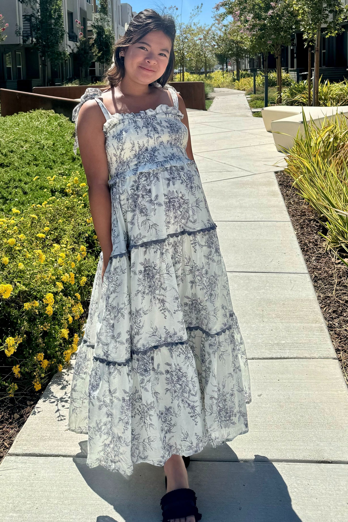 woman wearing a flowy white floral maternity dress with tiered detailing and a visible baby bump