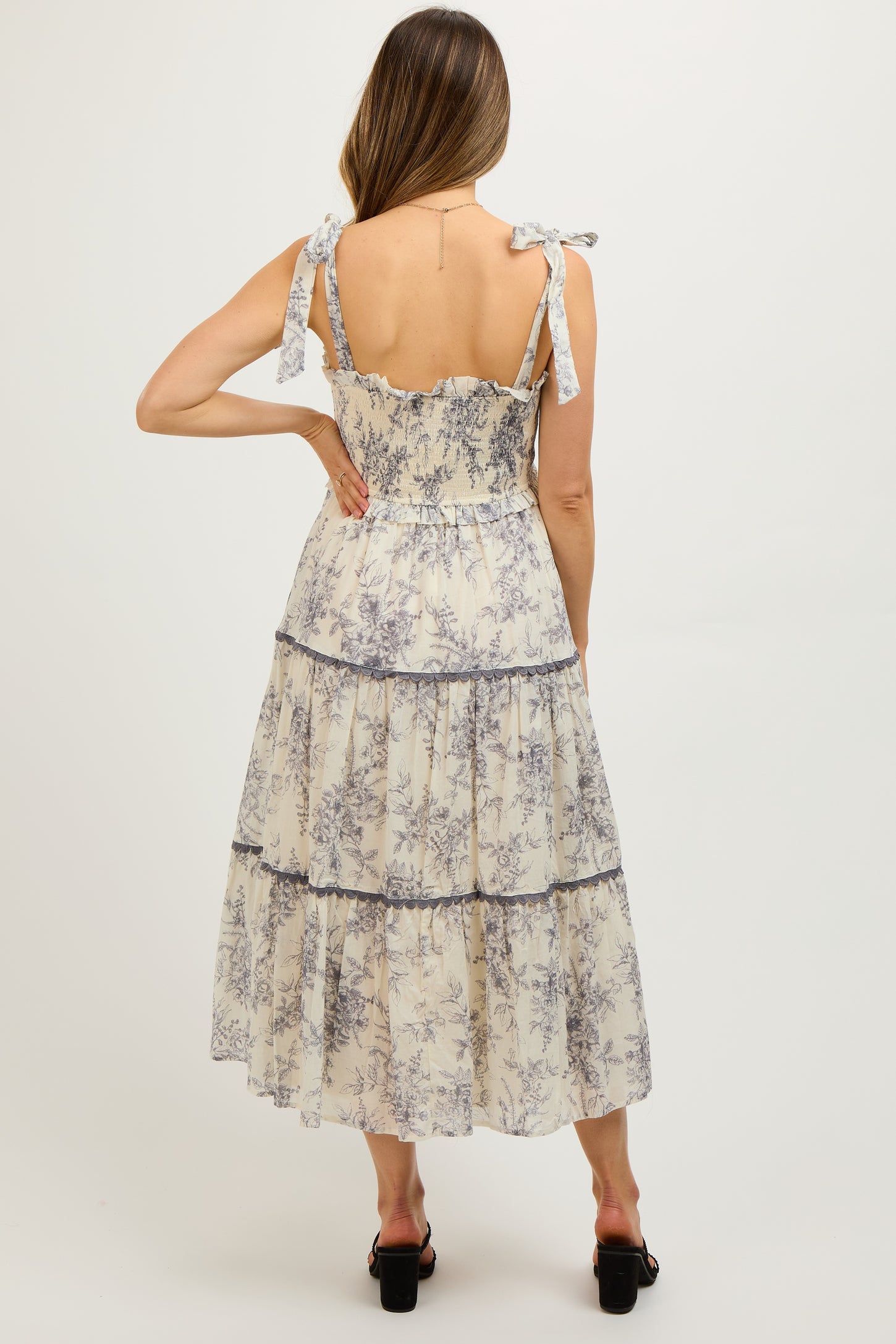 woman wearing a floral print maternity maxi dress with tie shoulder straps and a tiered skirt, shown from the back