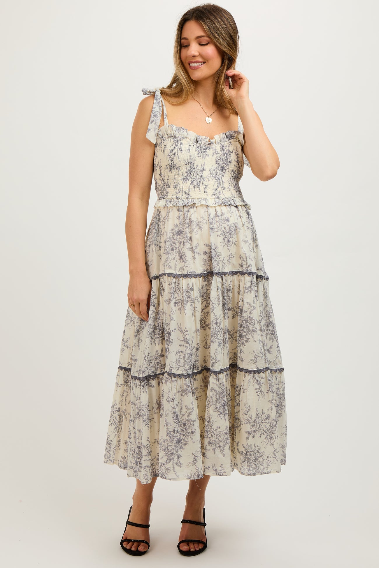 woman wearing a cream floral print maternity maxi dress with tiered layers and tie shoulder straps