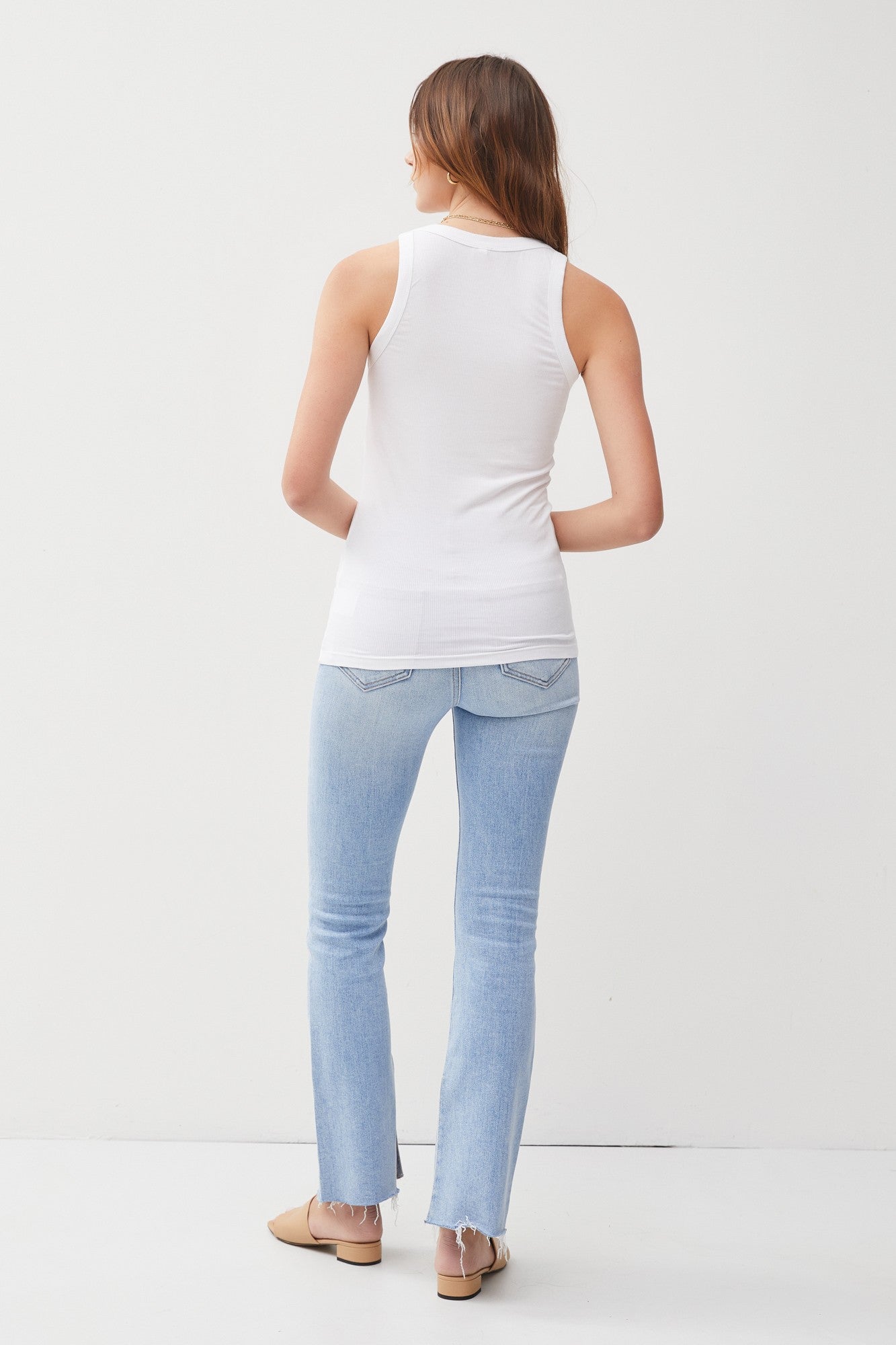 woman wearing a white ribbed tank top and light blue flared jeans, viewed from the back
