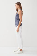 woman wearing a navy blue sleeveless top and white wide-leg pants with white sneakers, standing in profile