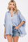 woman wearing a light blue striped oversized button-up shirt with rolled sleeves and distressed denim shorts