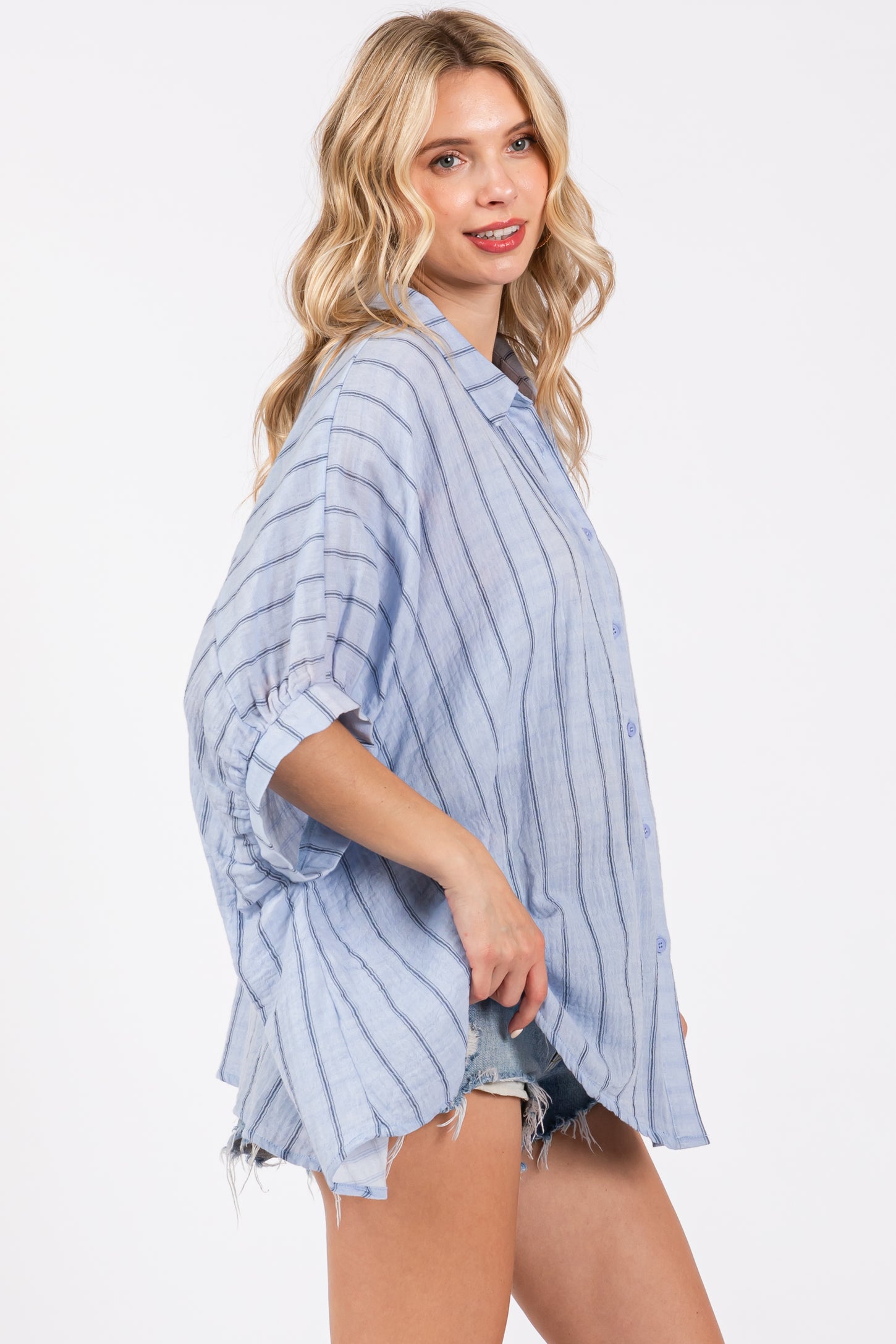 woman wearing a light blue striped oversized button-up shirt paired with denim shorts