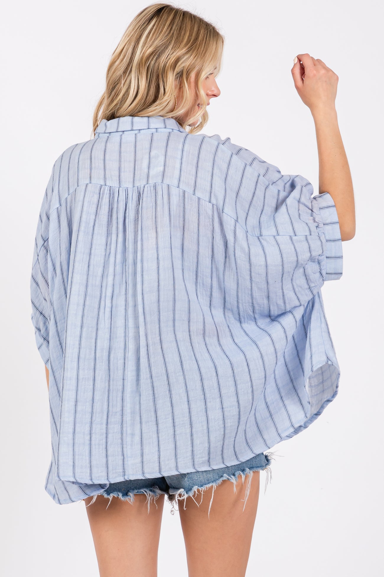 woman wearing a blue and white striped loose-fitting oversized shirt with rolled sleeves and a curved hem